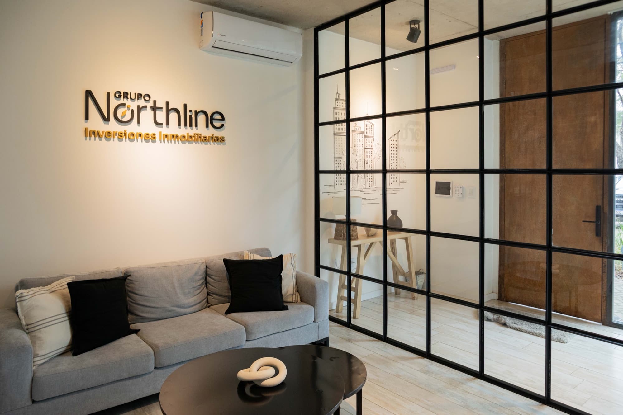 Recepción de Grupo Northline: sillón bajo el logo y mampara de hierro y vidrio
